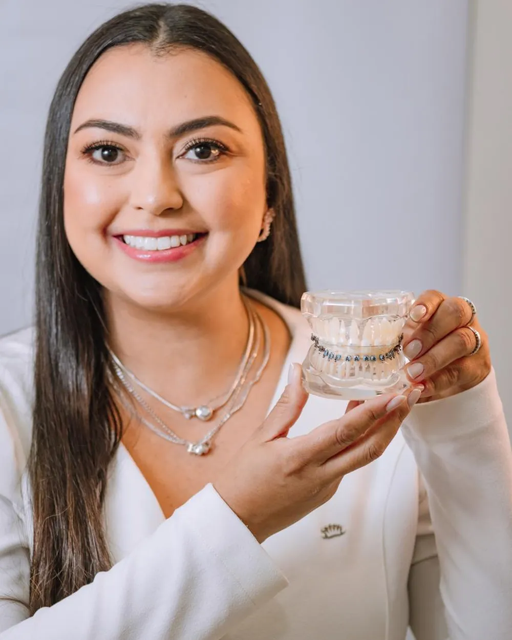 Dra. Rafaela Pierre sorrindo e segurando um modelo de arcada com aparelho