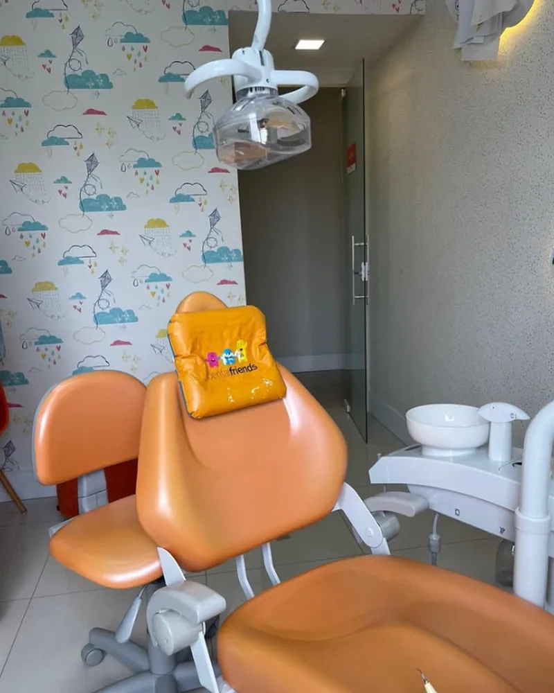 Consultório infantil da OrthoVip com cadeira odontológica laranja e papel de parede de nuvens e pipas