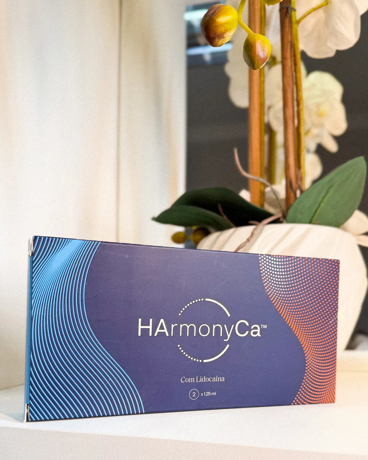Caixa do produto HArmonyCa ao lado de uma orquídea