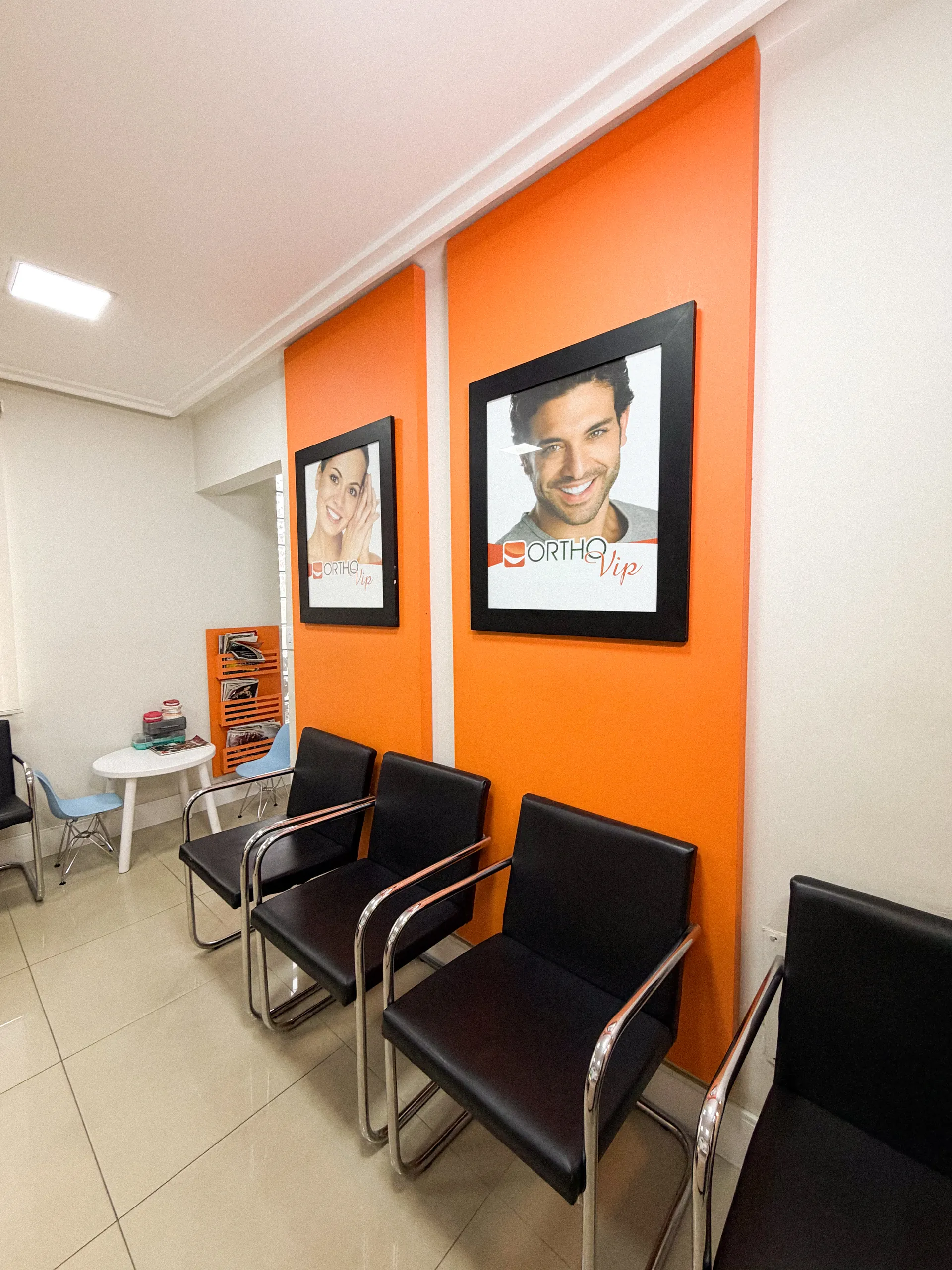 Sala de espera com parede laranja, cadeiras pretas e quadros de sorrisos